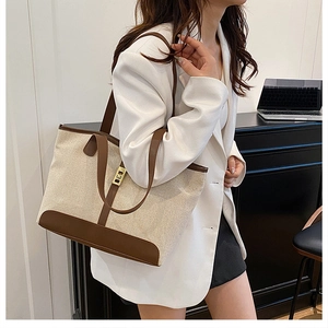 Detail of canvas tote bag with brown leather trim and golden metal turn-lock closure