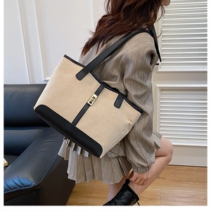 Close-up of contrast tote bag featuring beige canvas, black leather trim and gold metal lock