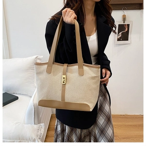 Detail of beige canvas tote bag with brown leather trim worn by a model in suit