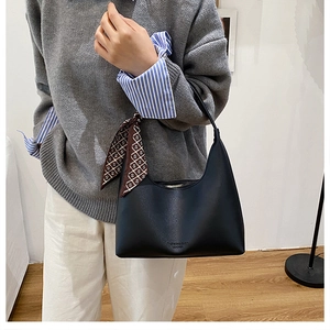 Détail d'un sac sous le bras en cuir noir avec un foulard en soie marron décoratif sur l'anse