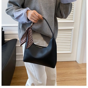 Close-up of black leather underarm bag featuring a stylish silk scarf handle detail