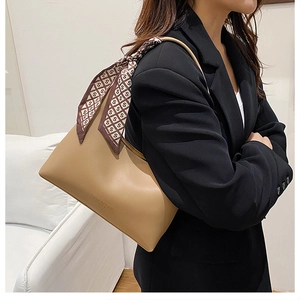 Close-up of khaki leather underarm bag with decorative silk scarf and logo detail