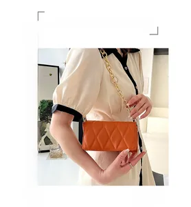 Detail of orange quilted crossbody bag with chunky gold chain strap worn by a model