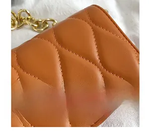 Macro detail of wave quilting on brown leather bag with thick golden metal chain strap