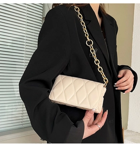 Close-up of beige quilted crossbody bag with chunky gold chain strap on black blazer