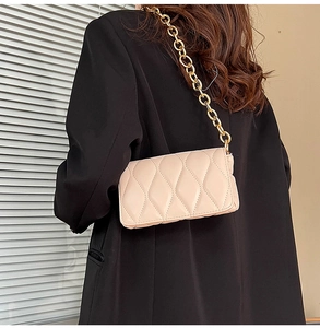 Quilted beige crossbody bag with chunky gold chain strap worn over a black blazer