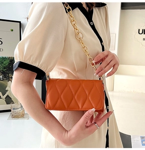 Detailed view of an orange quilted crossbody bag with chunky gold chain strap and texture