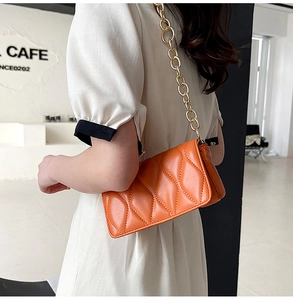Detail of orange quilted crossbody bag with chunky gold chain strap worn by a model