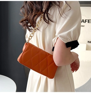 Detail of brown quilted shoulder bag with wavy stitching and chunky gold chain strap