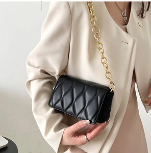 Detail of black quilted leather crossbody bag with chunky gold chain strap on model