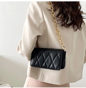 Detail of black quilted crossbody bag with a thick gold chain strap on a model shoulder
