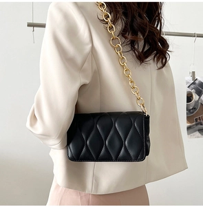 Detail of black quilted shoulder bag featuring gold chunky chain and wave stitching pattern