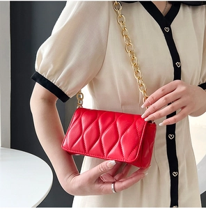 Detail of red quilted crossbody bag with gold chain strap shown on a model side