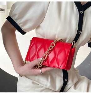 Detail of red quilted square crossbody bag with chunky gold chain strap and flap closure