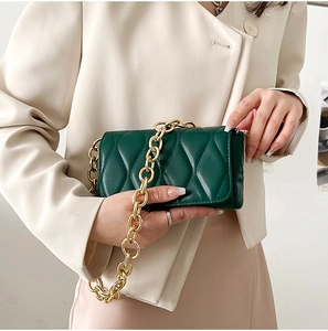 Detail of dark green quilted crossbody bag with chunky gold chain on white blazer