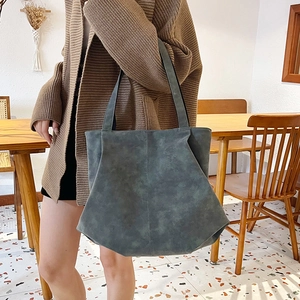 Deep green large capacity tote bag with unique geometric cut worn with a brown cardigan