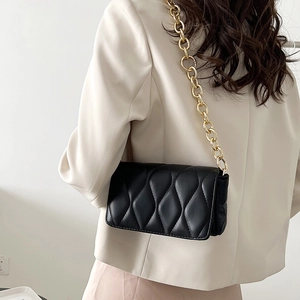 Minimalist black quilted shoulder bag with chunky gold chain strap worn with stylish outfit