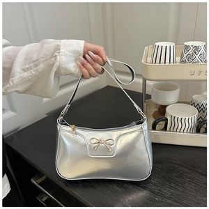 Detailed close-up of metallic silver underarm bag with a delicate golden bow decoration