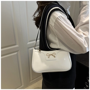Side view of a white patent leather shoulder bag with a gold metal bow on a model