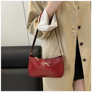 Detalle de bolso baguette de charol rojo con lazo de metal dorado y superficie lisa
