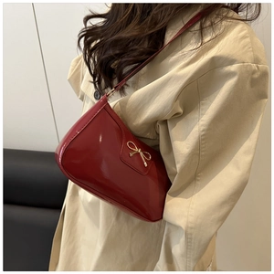 Detail of red patent leather underarm bag featuring a golden metal bow pendant