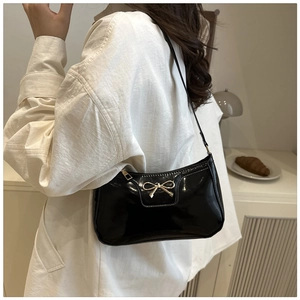 Close-up of a black patent leather shoulder bag featuring a golden bow metal buckle