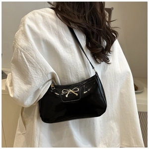 Detalle de bolso de hombro en charol negro brillante con adorno de lazo dorado
