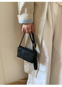 Detail of black woven leather square bag featuring a distinctive gold triangle metal buckle