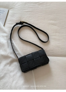 Close-up of black woven texture on a minimalist rectangular flap bag with gold buckle detail