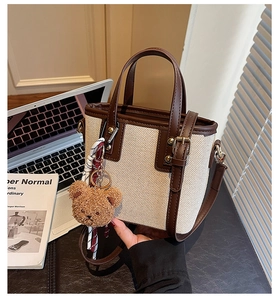 Détail du sac seau en toile crème avec finitions en cuir marron et breloque ours