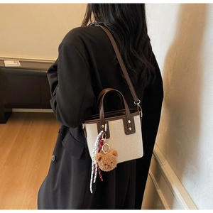 Détail du sac seau en toile avec garniture en cuir marron, ours en peluche et foulard