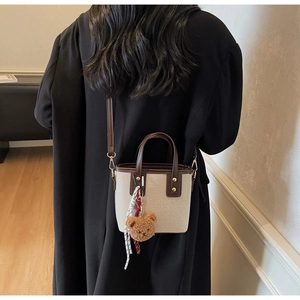 Sac seau en toile et cuir marron avec breloque ours porté en bandoulière par le modèle