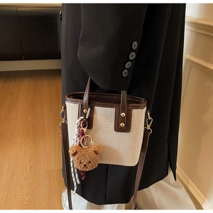 Détail du sac seau en toile avec finitions cuir et breloque ours porté avec un blazer