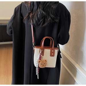 Détail du sac seau en toile avec bordure en cuir marron, breloque ours et glands tissés