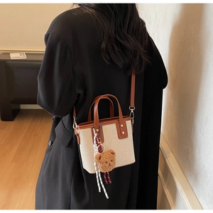 Détail du sac seau en toile avec finitions en cuir marron et breloque ours sur modèle