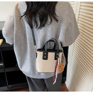 Détail du sac seau en toile avec finitions cuir, breloque ours et bandoulière amovible