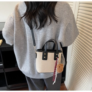 Détail d'un sac seau en toile beige avec garniture en cuir noir et pendentif ours
