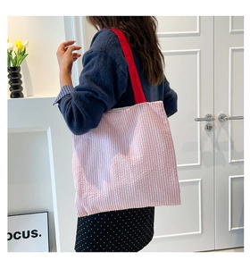 Detail of pink striped tote bag with red shoulder straps worn by model in minimalist room