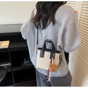 Détail du sac bandoulière en toile beige avec bordure en cuir noir et breloque ours