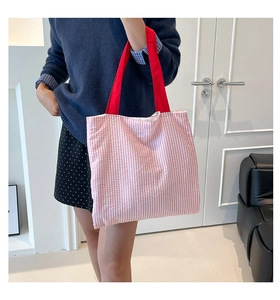 Détail d'un sac cabas en toile rayée avec anses rouges porté par un mannequin femme
