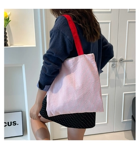 Pink striped tote bag with contrast red shoulder straps worn by model against white wall