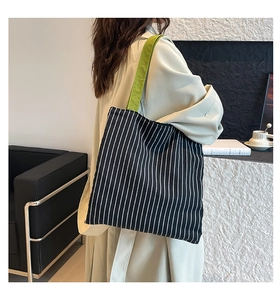 Detail of black and white striped tote bag with vibrant green straps on a female model