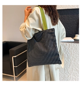 Detail of a large black and white striped canvas tote bag with vibrant green shoulder straps