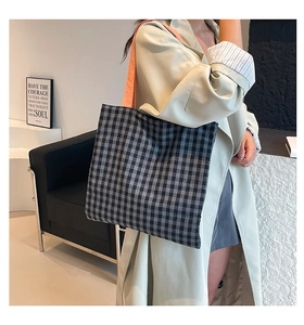 Detail of checkered tote bag featuring a contrasting orange strap on a model's shoulder