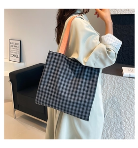 Detail of checkered shoulder bag with vibrant orange-pink strap held by a model