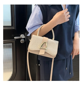 Close-up of beige textured handbag with glittering finish and gold horseshoe buckle detail