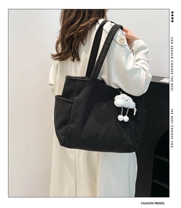 Detail of black corduroy tote bag featuring a soft white cloud plush pendant accessory