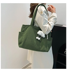 Detail of dark green corduroy tote bag featuring a cute white cloud plush pendant