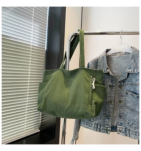 Detail of green corduroy tote bag featuring a decorative zipper and side pocket