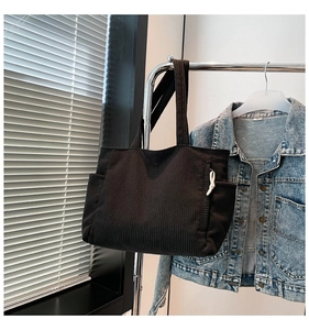 Detail of dark corduroy tote bag with side pocket and drawstring on a metal hanger